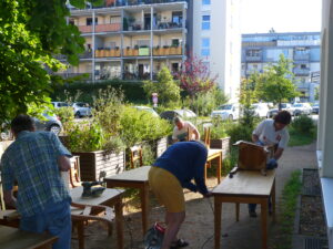Mehr über den Artikel erfahren Quartier: Sparkassen-Mitarbeiter vollenden Aufarbeitung von Tischen und Stühlen für neuen sozialen Treffpunkt